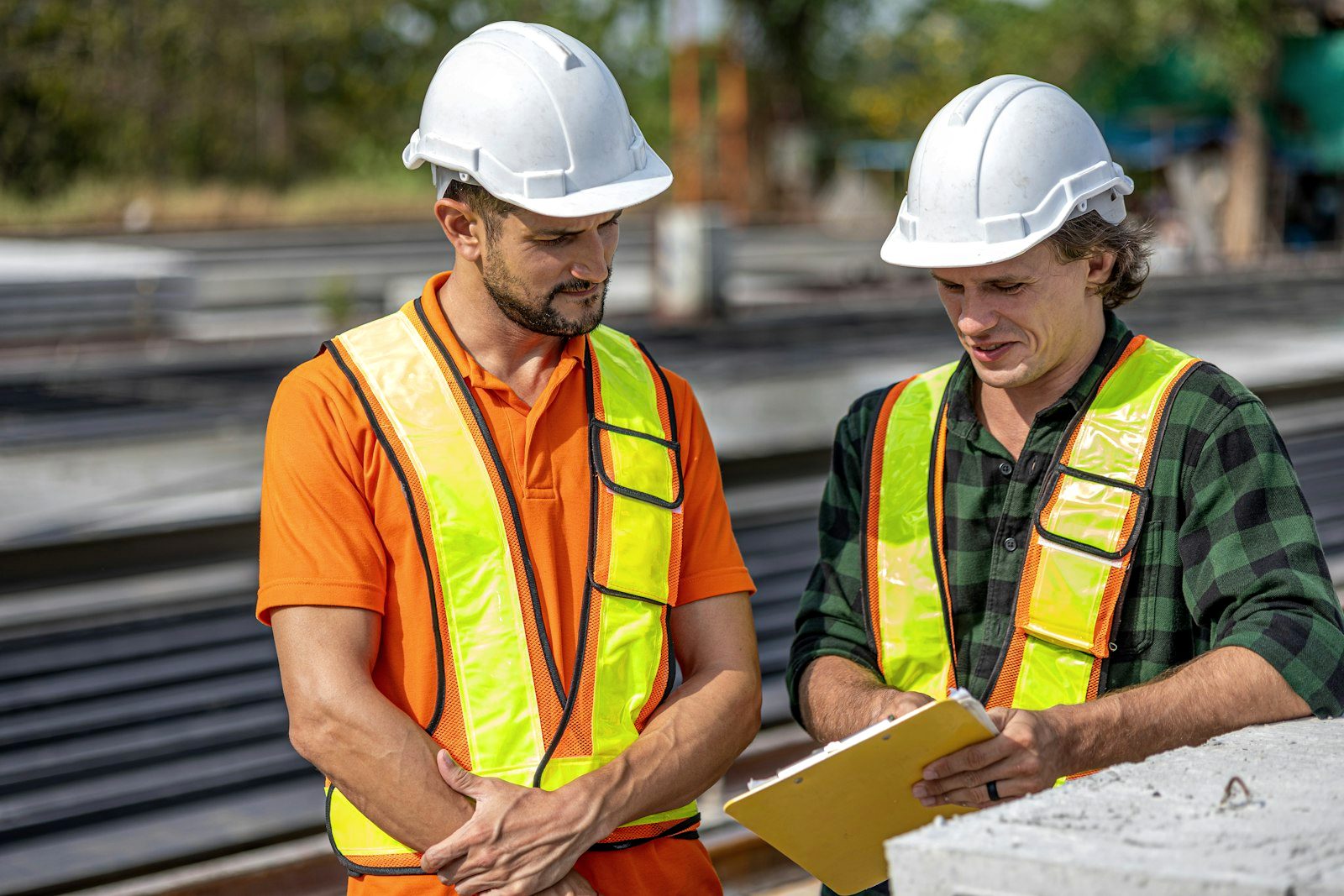 Two site supervisors in hi-vis and hard hats reviewing plans on a job site